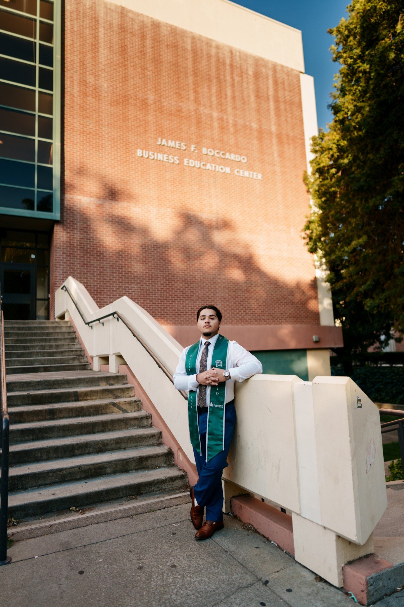 SJSU graduate in green Forest Systems Fund stole leans against the concrete railing at James F. Boccardo Business Education C