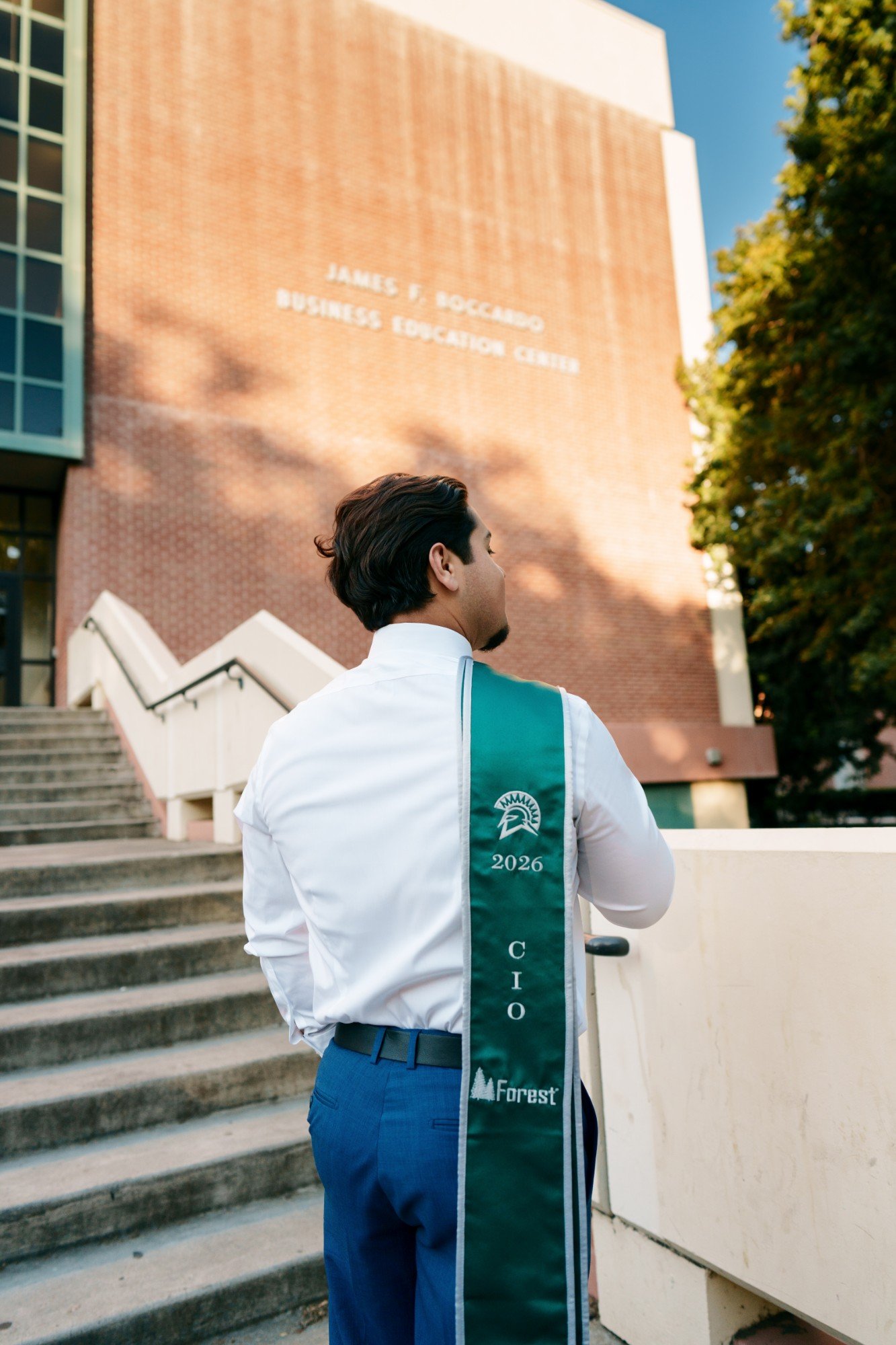 Back view of SJSU 2026 CIO grad showing his green Forest stole facing the Boccardo Business Education Center