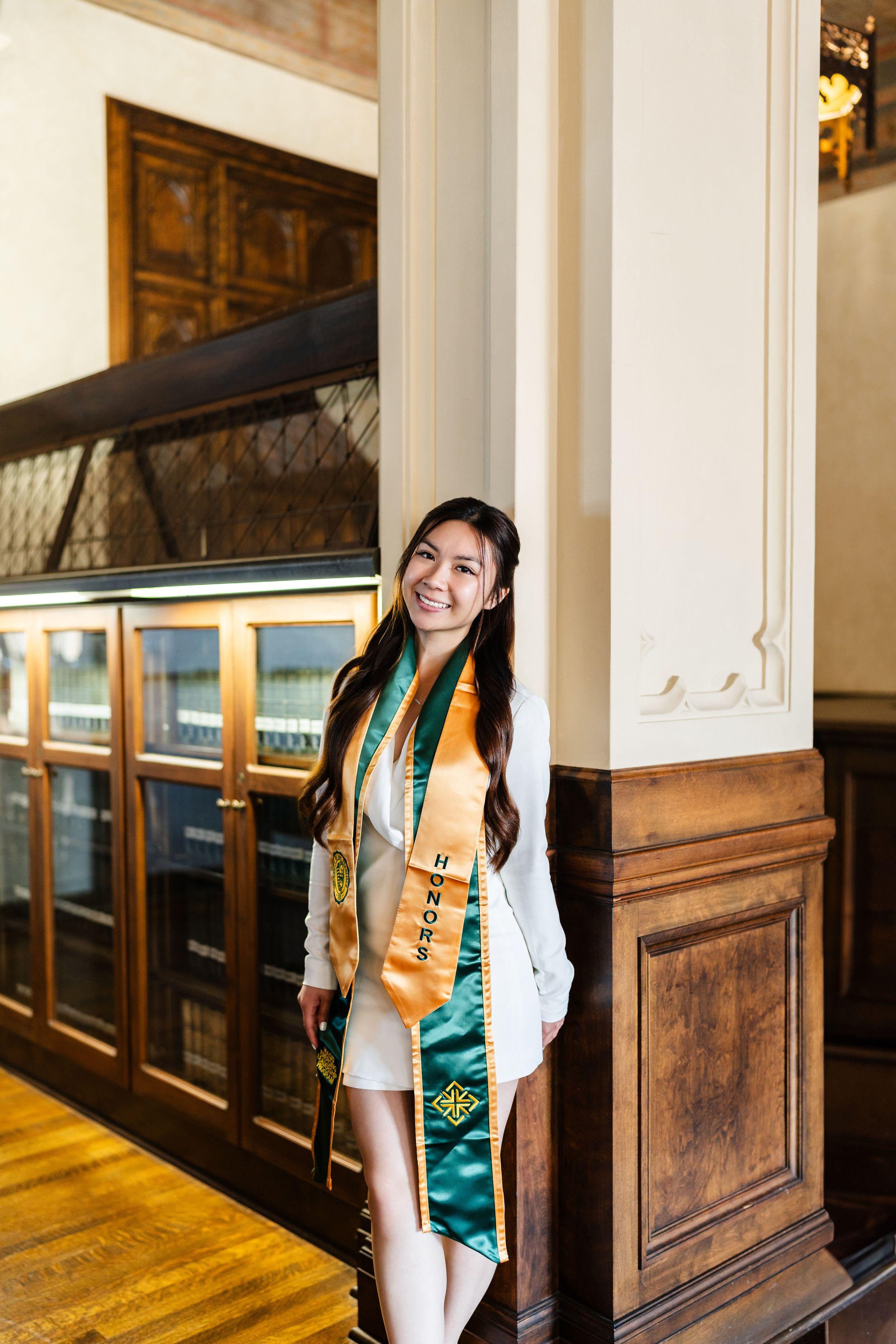 USF graduate poses in cap and gown during golden hour on the University of San Francisco campus