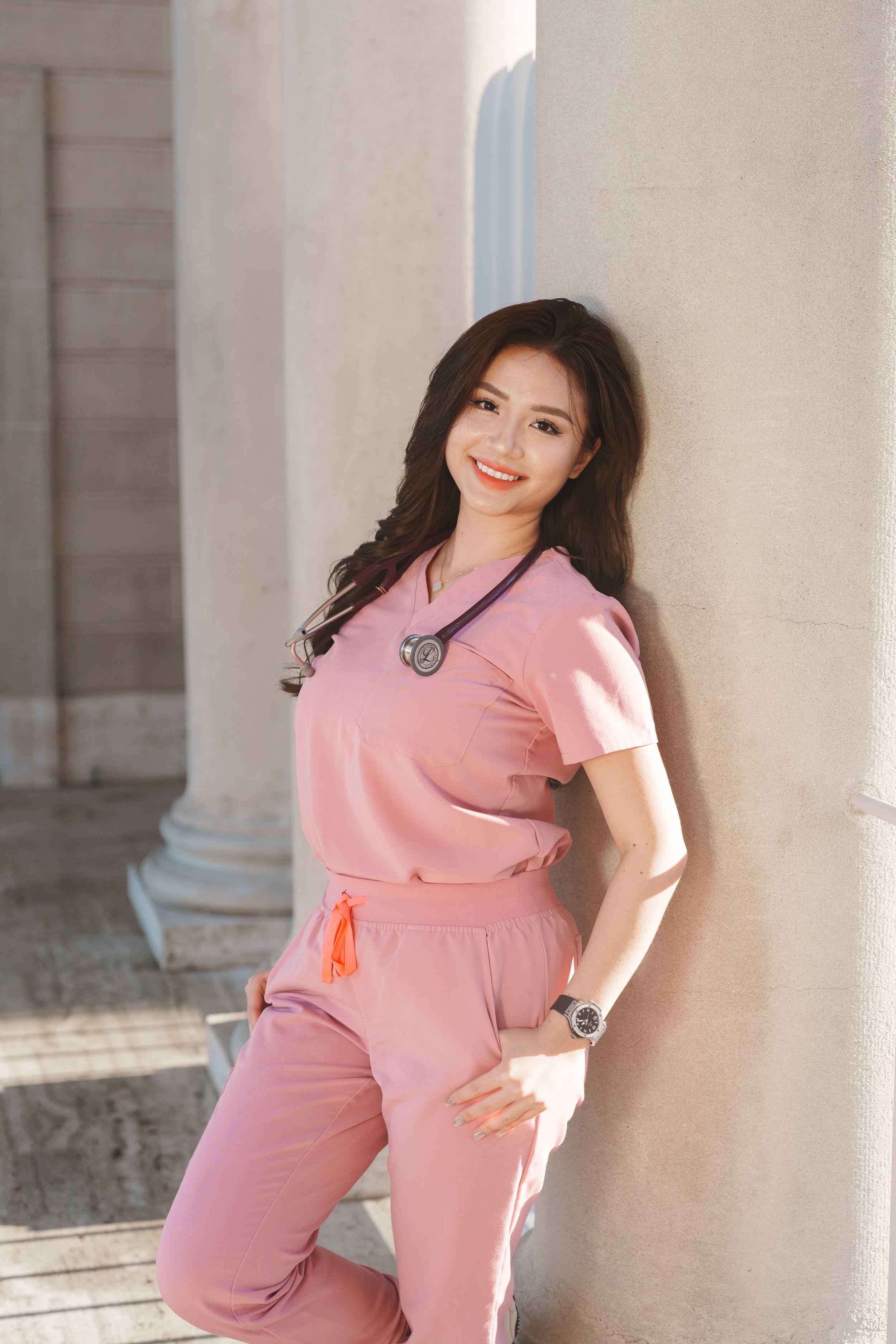 SF State nursing graduate in pink scrubs with stethoscope leaning against a stone column at the Legion of Honor