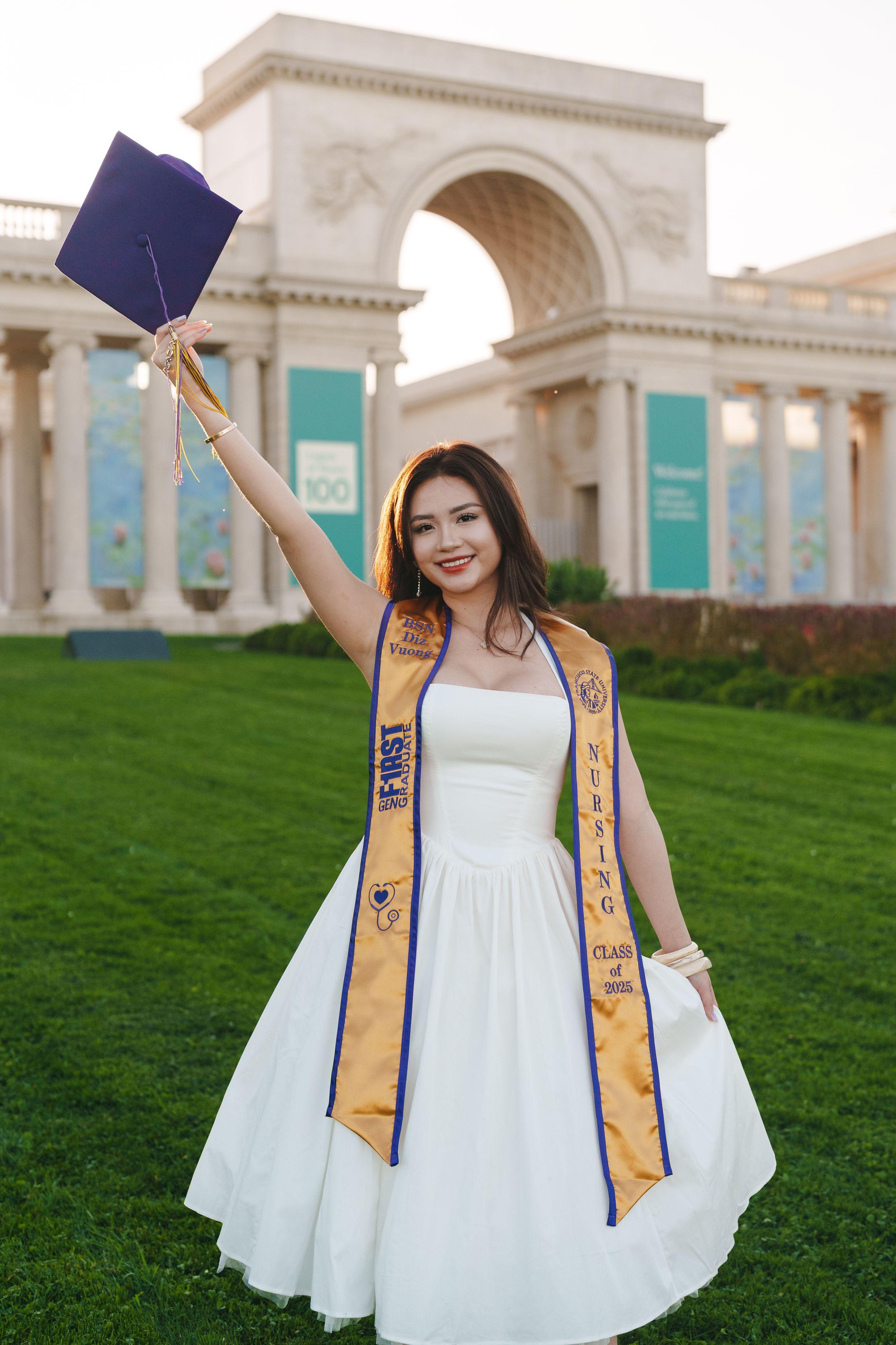 SF State BSN graduate in white dress and gold stole lifting her cap at the Legion of Honor archway at golden hour