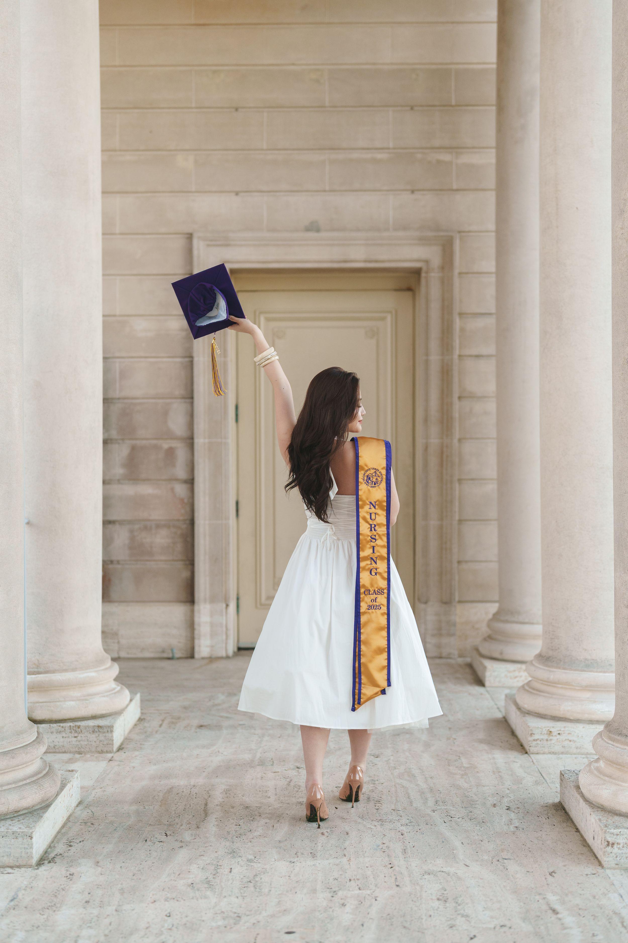 SF State graduate posing in cap and gown at the Legion of Honor during golden hour in San Francisco