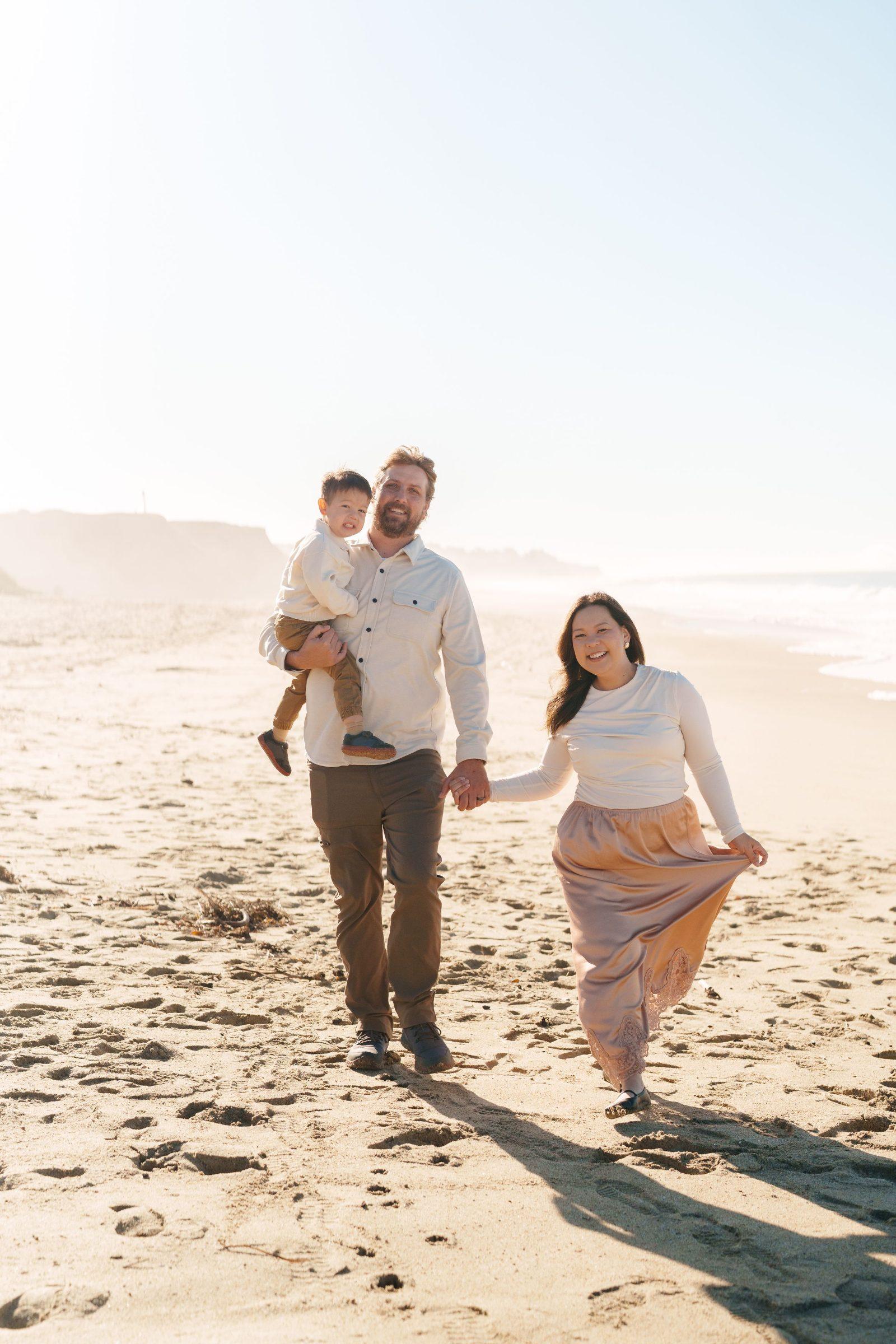 Bay Area family portrait of dad holding young son while holding hands with mom in blush skirt on sandy beach at golden hour.