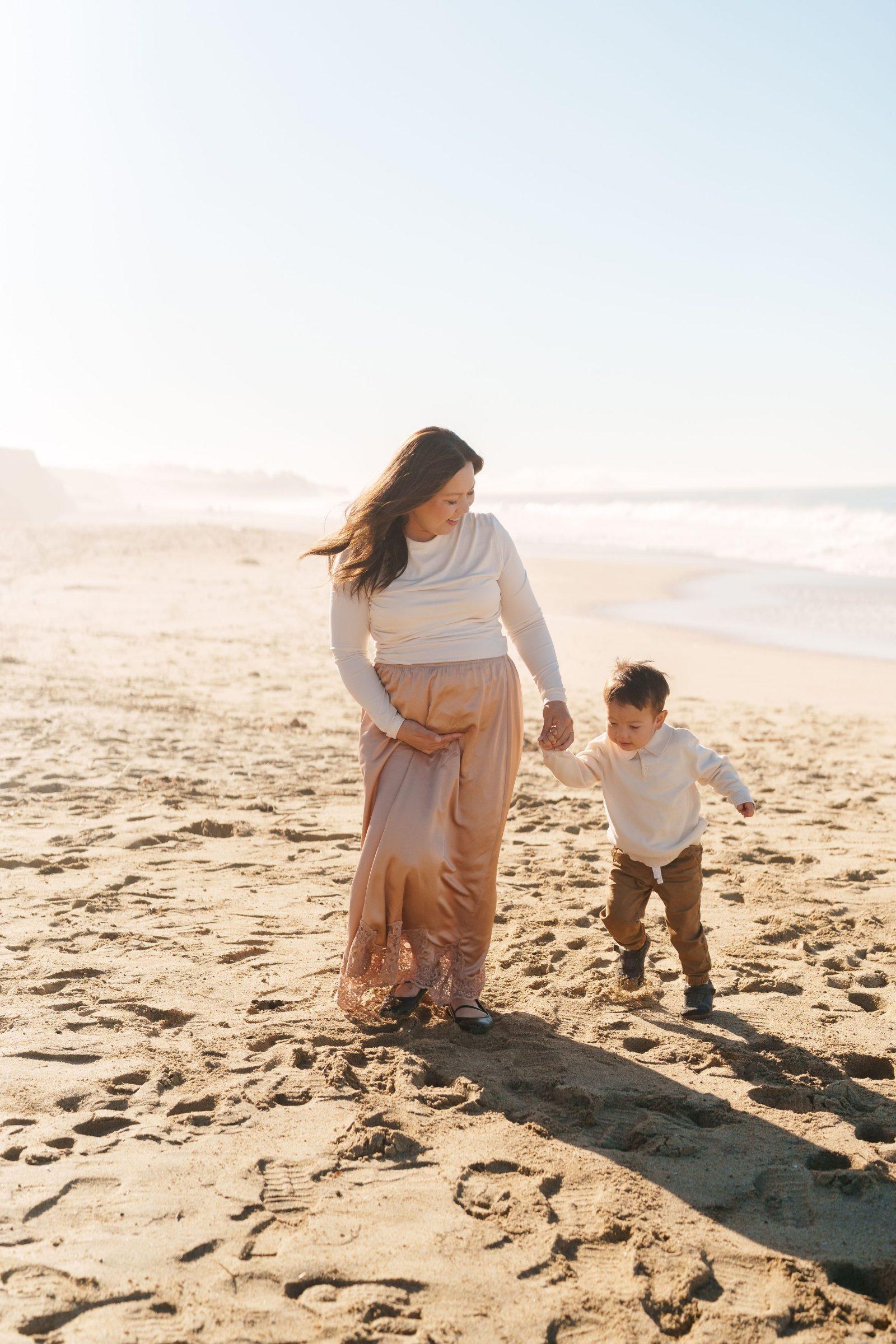 Bay Area family portrait of an expecting mother in a cream top and blush satin skirt holding her toddler son's hand on a