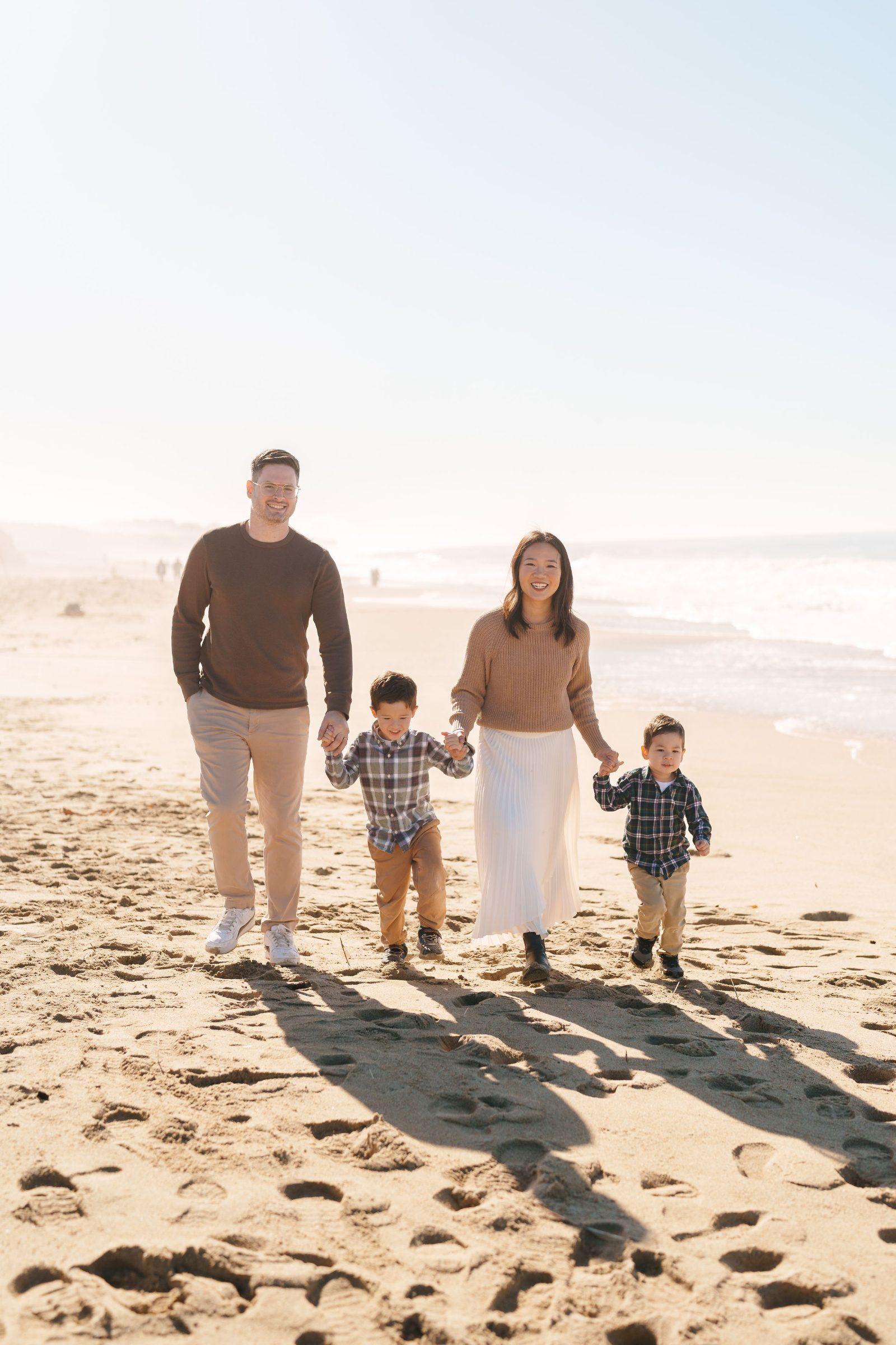 Bay Area family portrait of parents and two young boys in plaid shirts and earth tones holding hands while walking on sandy
