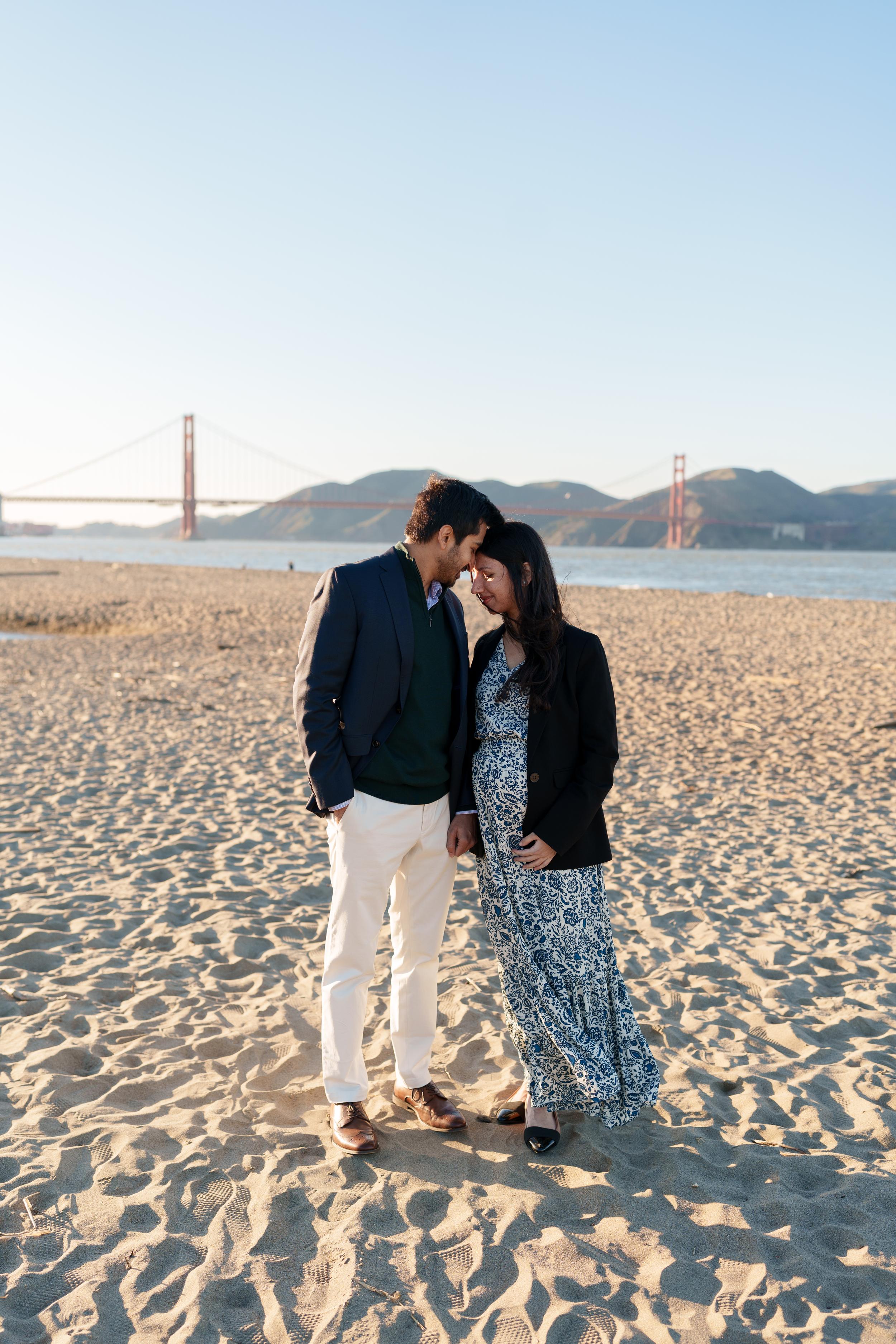 Bay Area couples portrait of a man in navy blazer and woman in blue floral dress touching foreheads on Crissy Field sand.