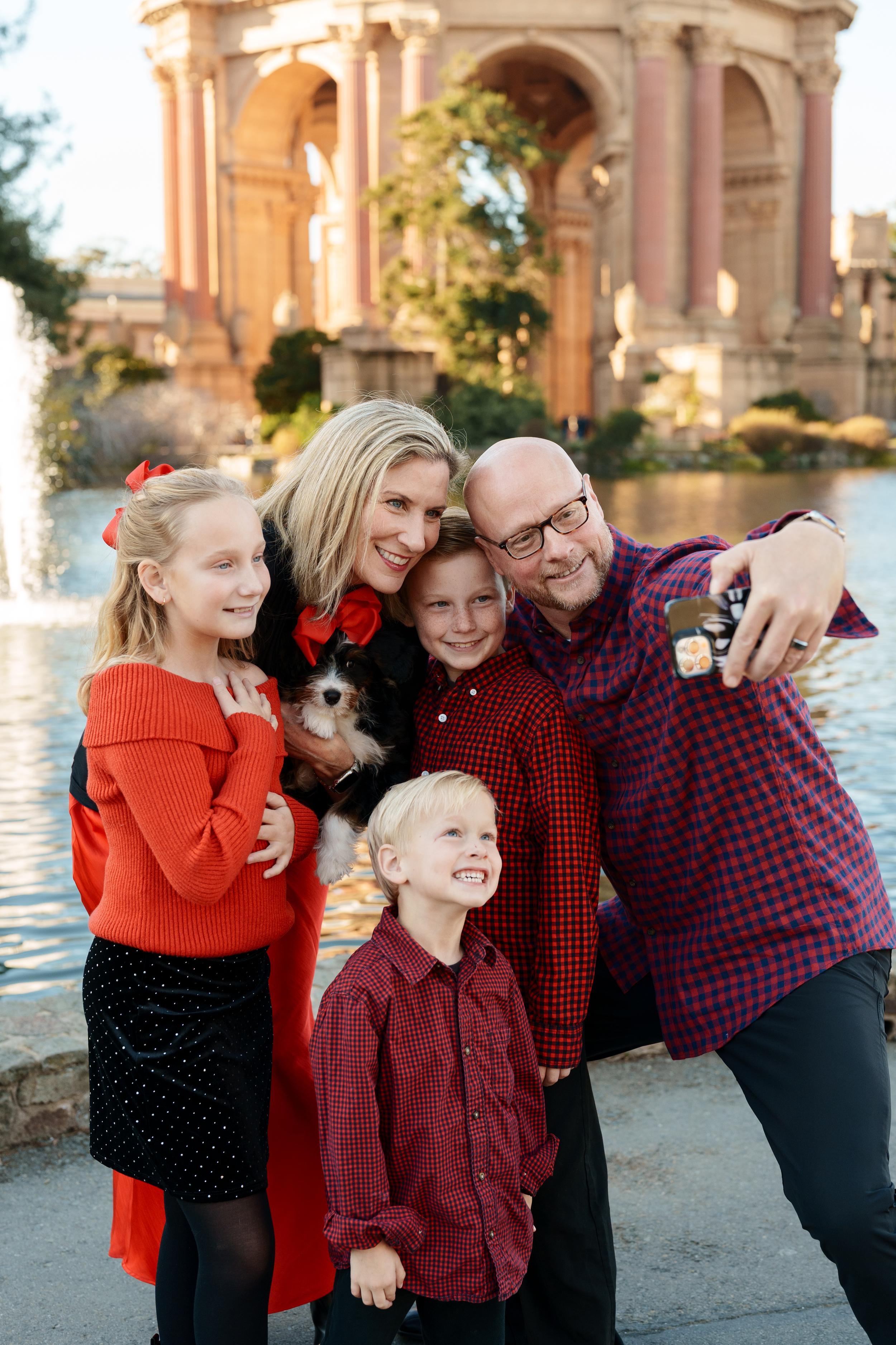 Bay Area family portrait selfie in red and black plaid at Palace of Fine Arts, parents with three kids and a puppy by the