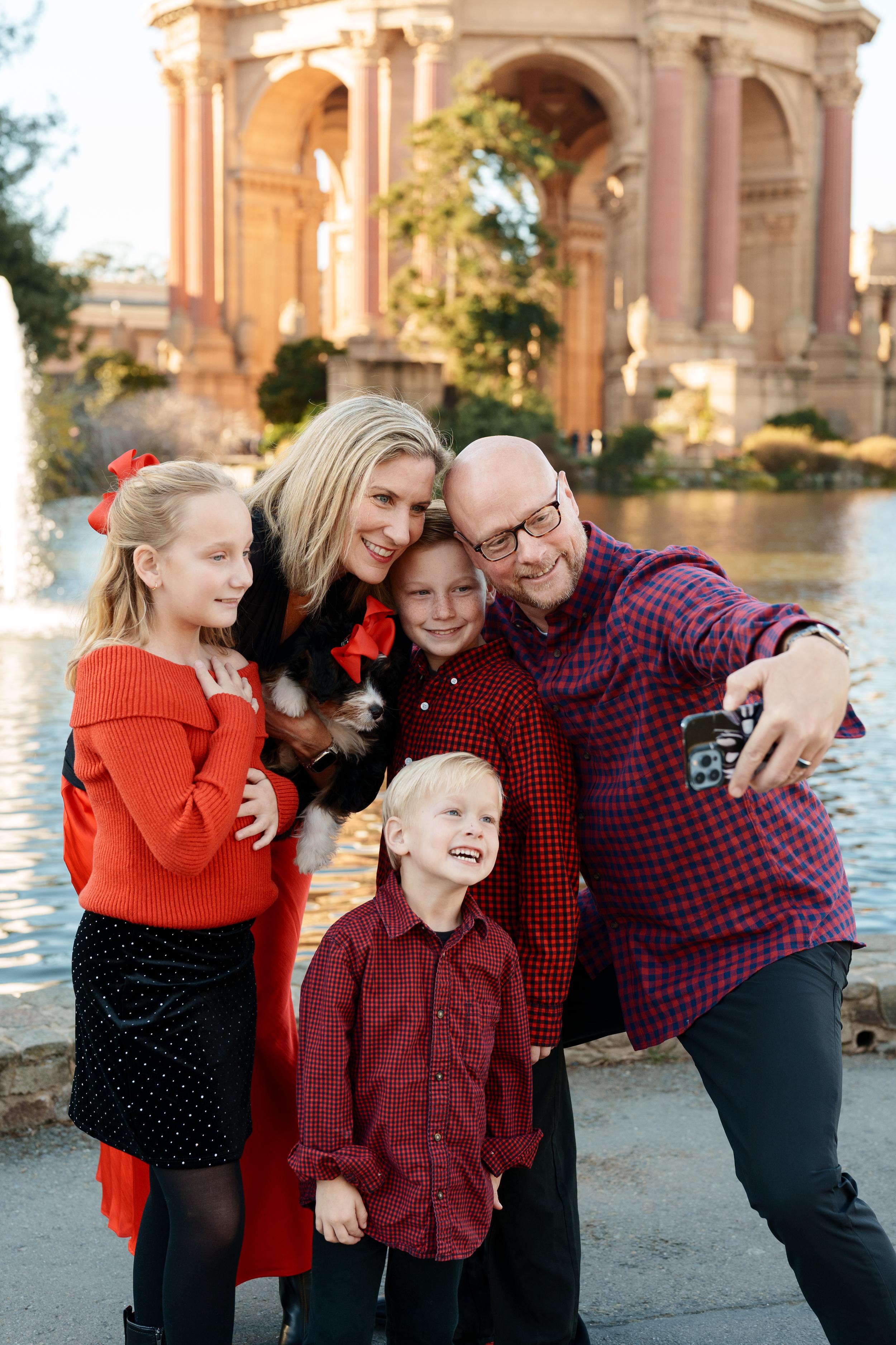 Bay Area family portrait of parents, three kids in red, and a puppy taking a selfie at San Francisco's Palace of Fine Arts.