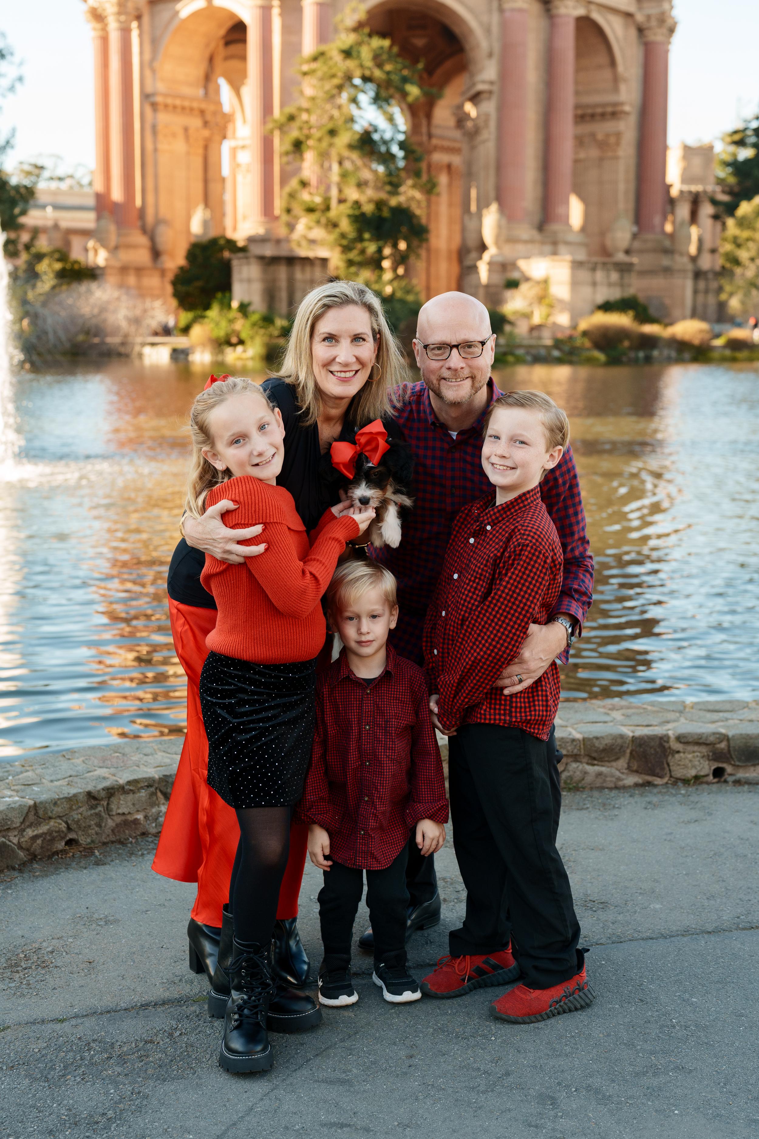 Bay Area family portrait of parents, two boys and a daughter in red and black holding a puppy at the Palace of Fine Arts
