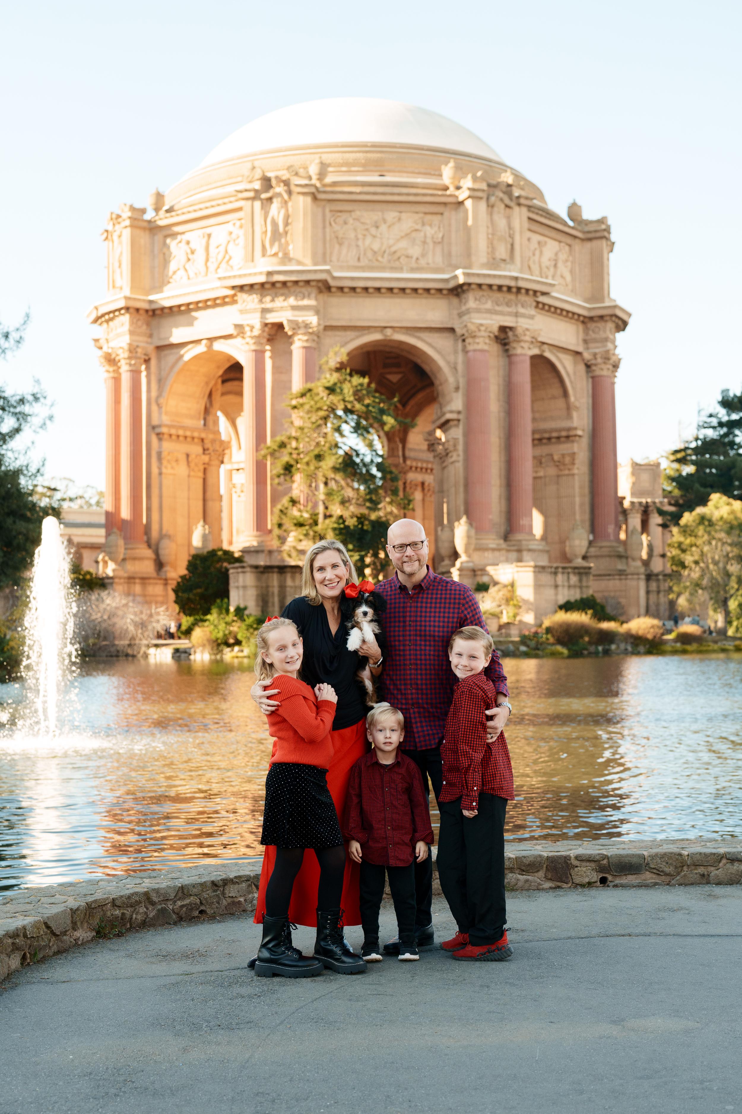 Bay Area family portrait of parents, three kids and a puppy in red and black attire by the Palace of Fine Arts lagoon at