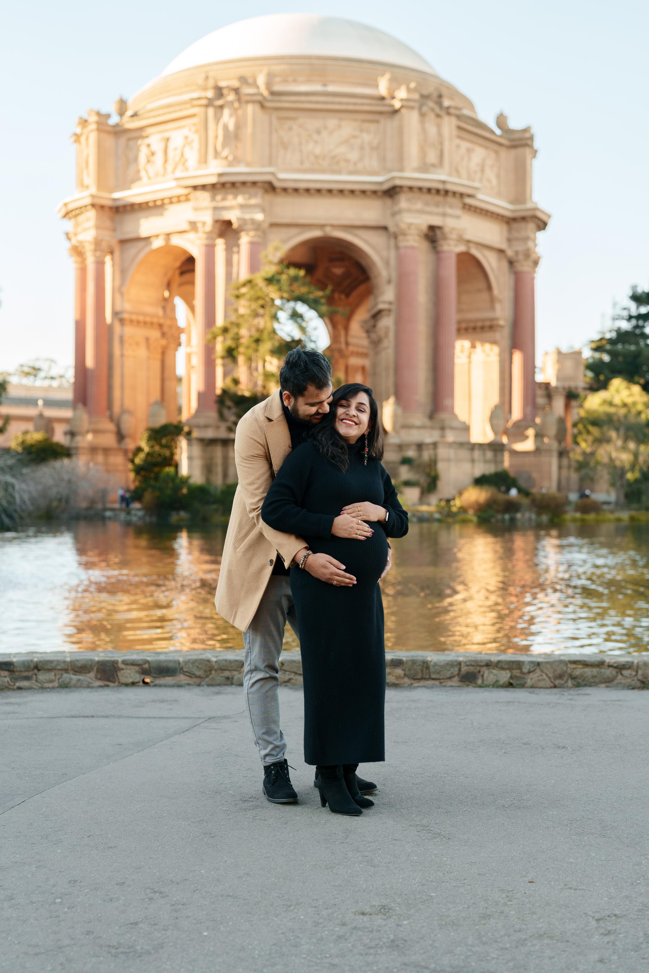 Bay Area couples portrait of an expecting couple embracing in front of the Palace of Fine Arts rotunda and lagoon at golden