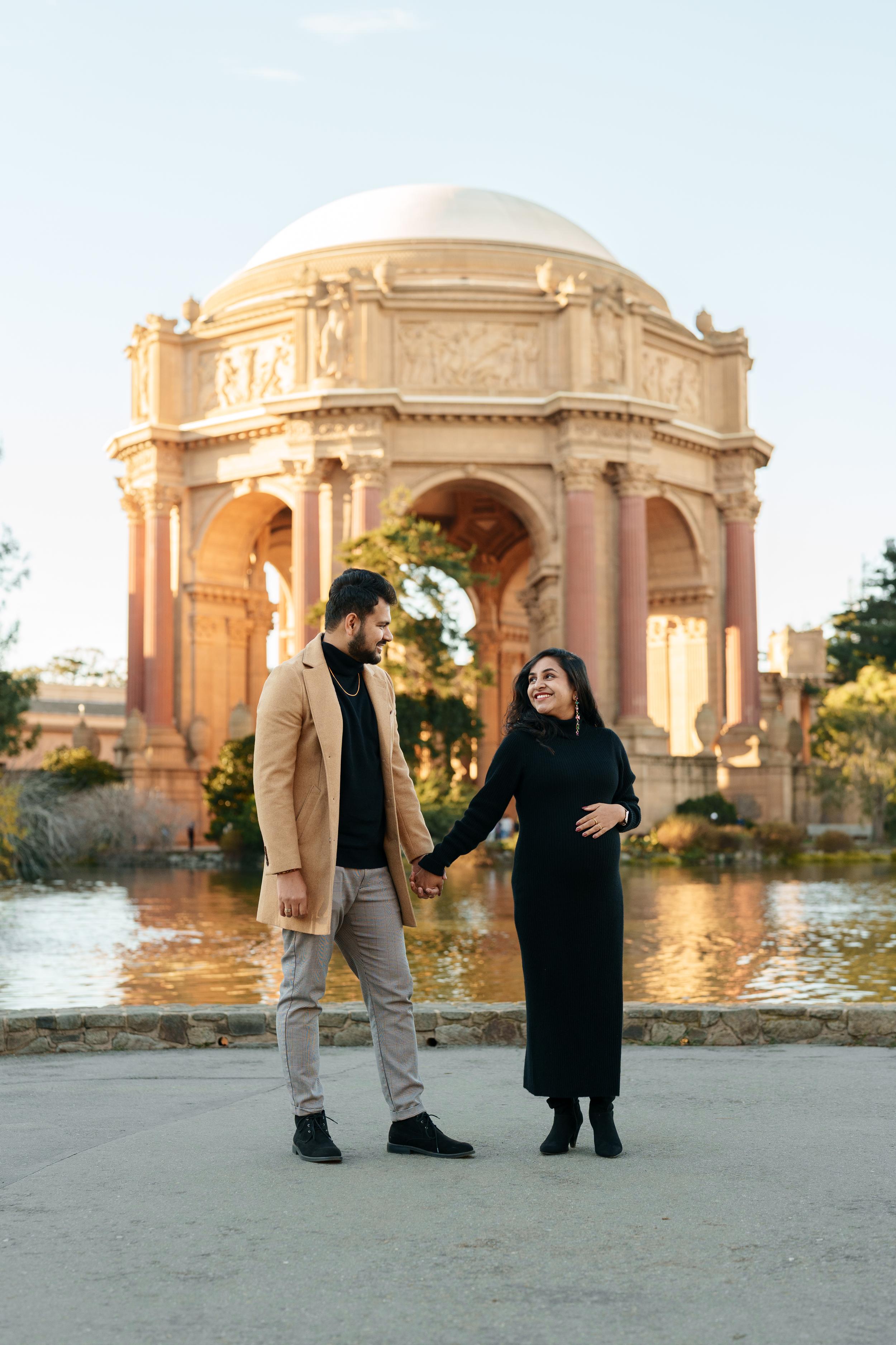 Bay Area couples portrait of an expecting couple holding hands at the Palace of Fine Arts rotunda, glowing in golden hour