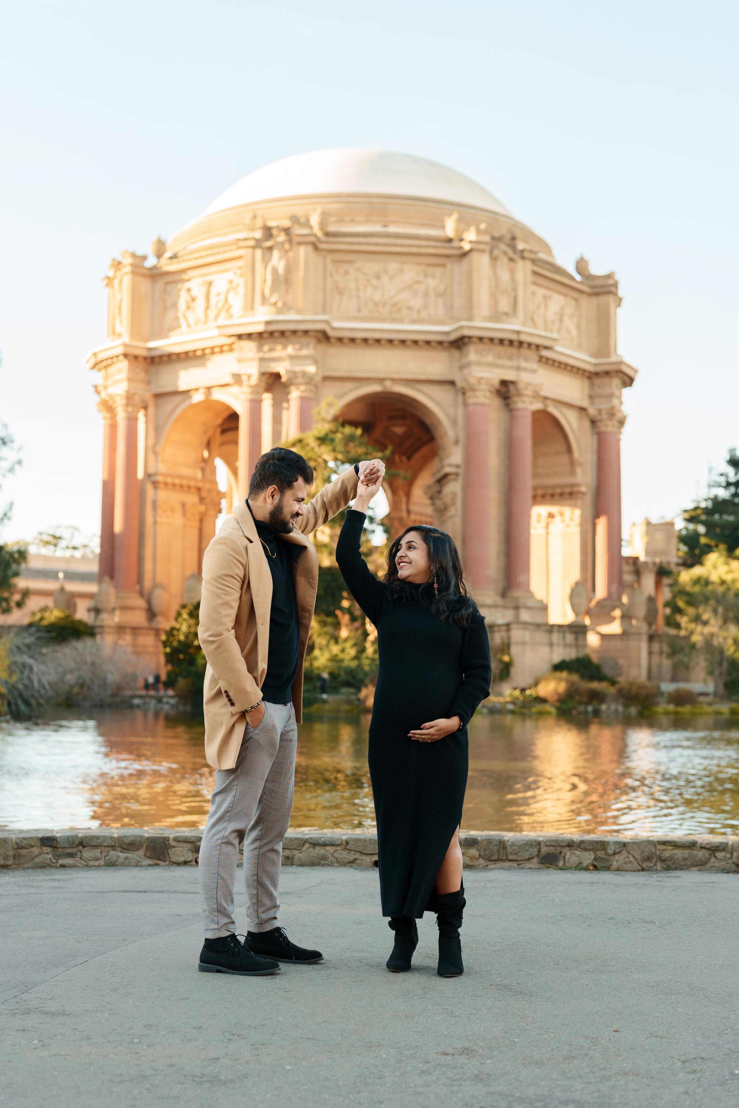 Bay Area couples portrait of an expecting couple twirling by the lagoon at the Palace of Fine Arts in golden hour light.