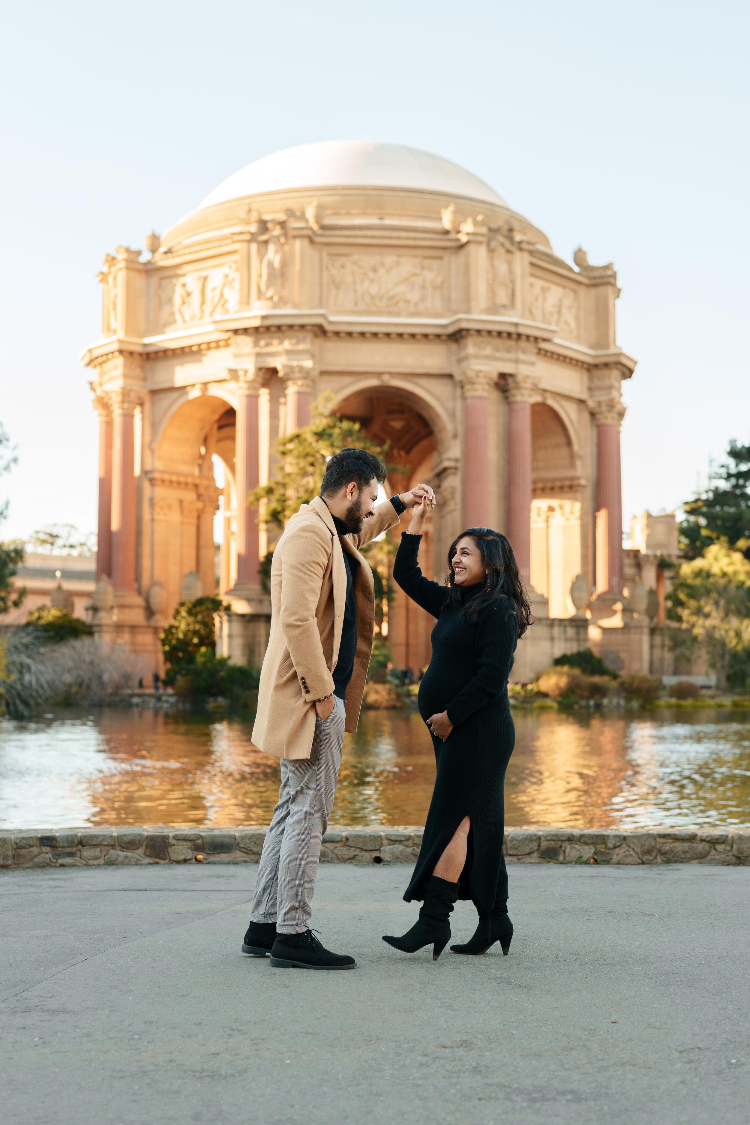 Bay Area couples portrait of expecting partners twirling in front of the Palace of Fine Arts rotunda at golden hour.