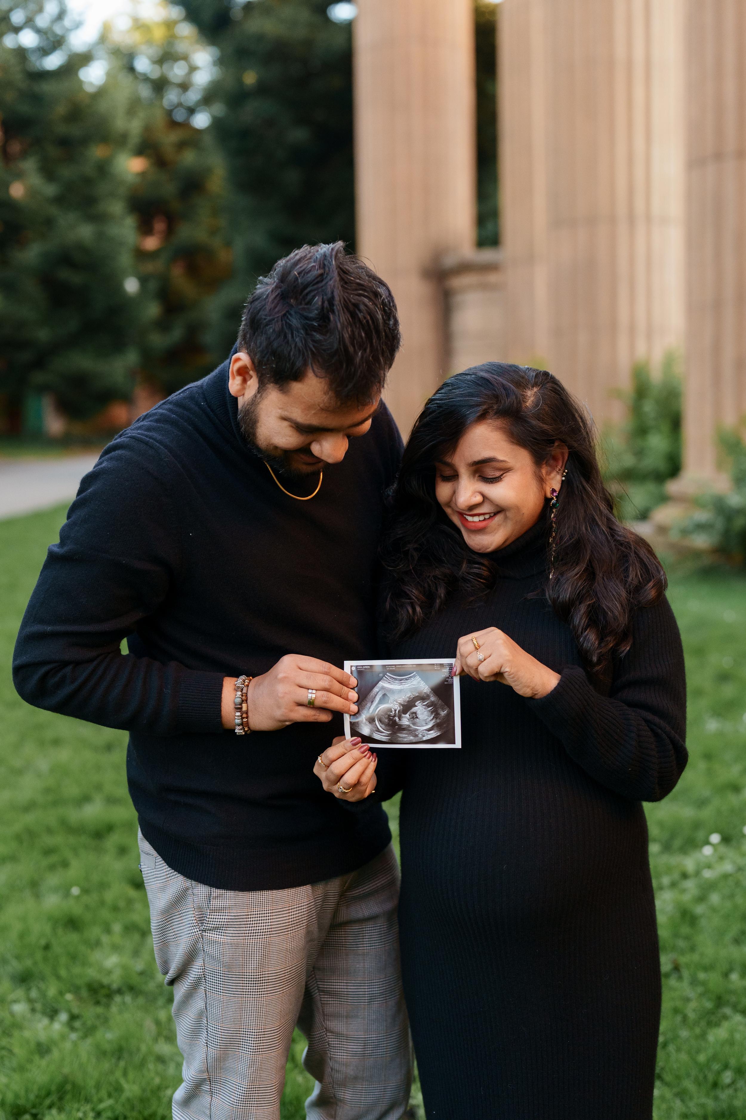 Bay Area couples portrait of expecting parents in black sweaters holding an ultrasound photo near the Palace of Fine Arts