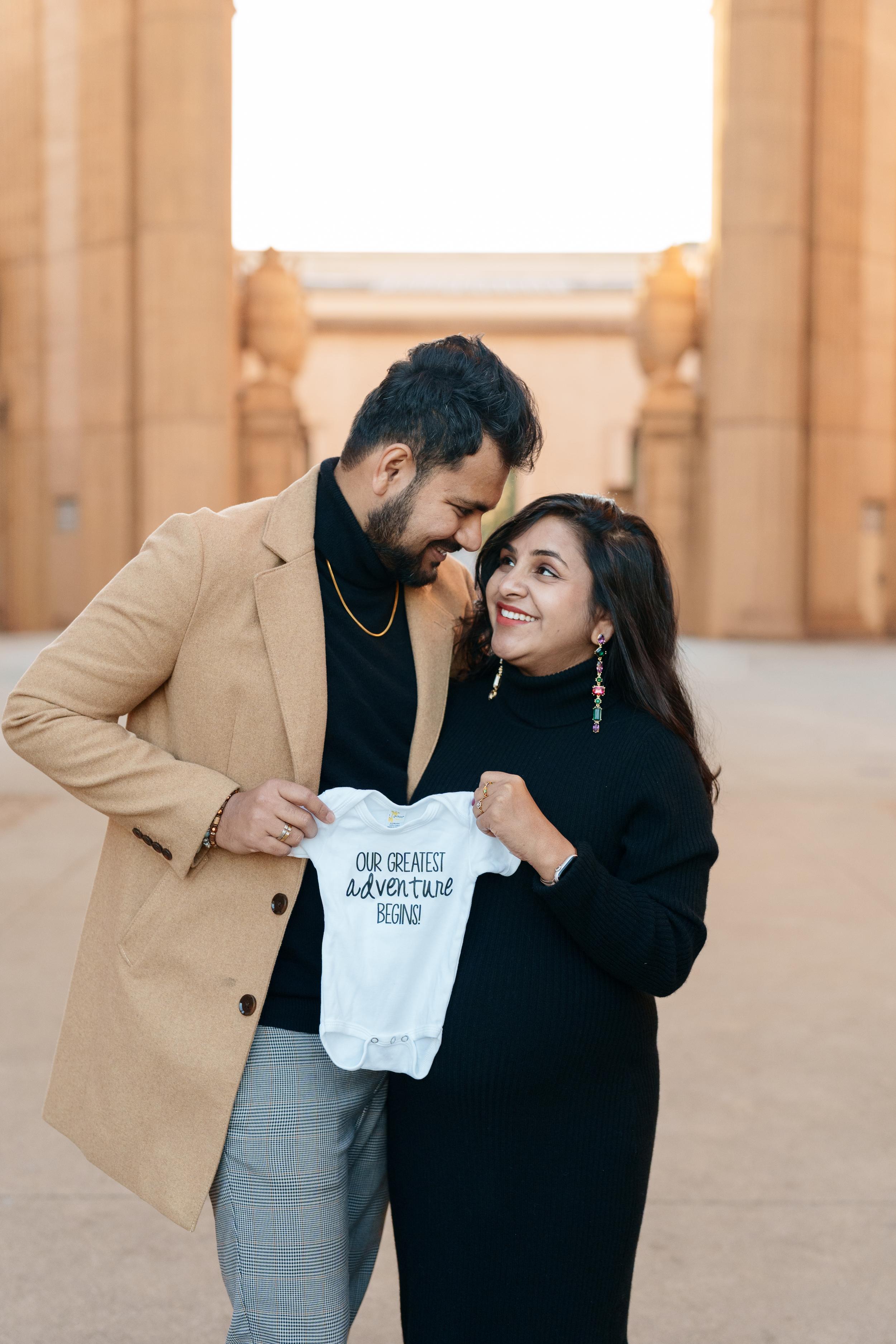 Bay Area couples portrait of expecting parents holding a baby onesie at the Palace of Fine Arts columns at sunset.