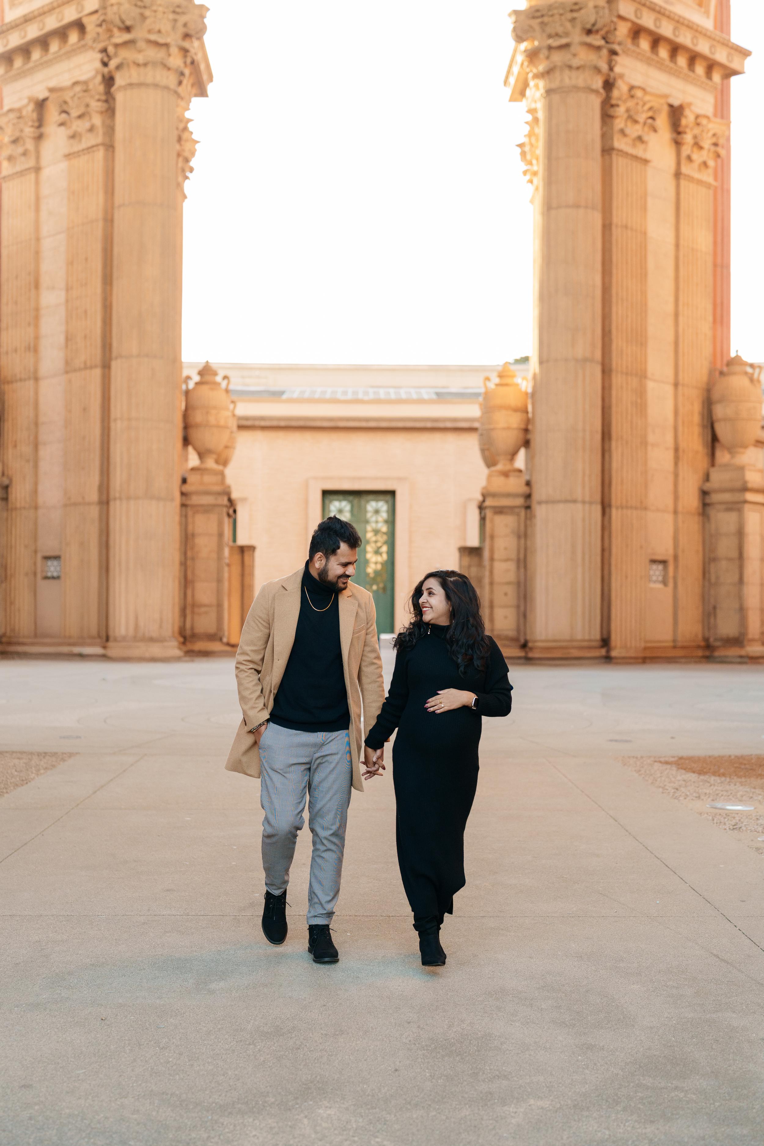 Bay Area couples portrait of a smiling pair holding hands between towering columns at the Palace of Fine Arts, she in a long