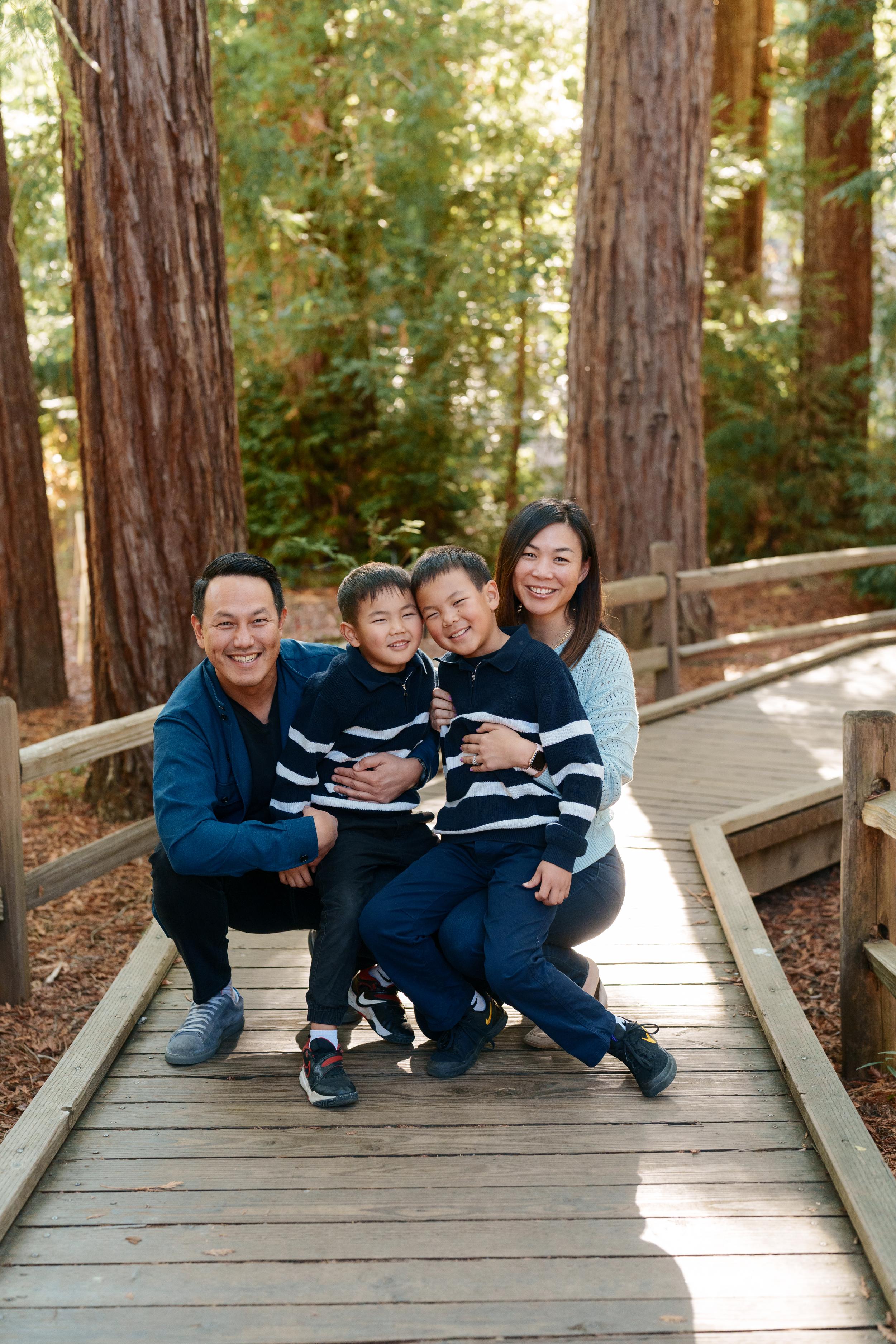 Bay Area family portrait of parents crouching with two young sons in matching navy striped sweaters on a wooden boardwalk